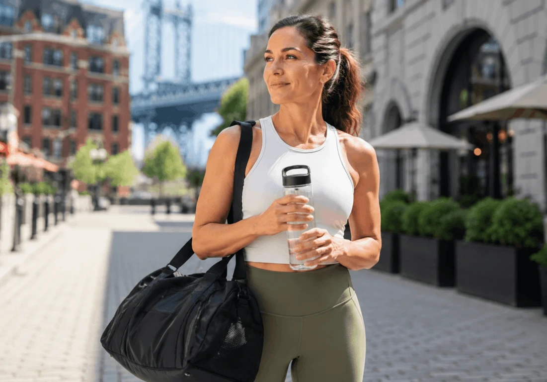 Person in athletic wear walking through the city with a gym bag and water bottle